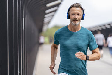 Sportlicher Mann, der Kopfhörer trägt und joggt - DIGF07492
