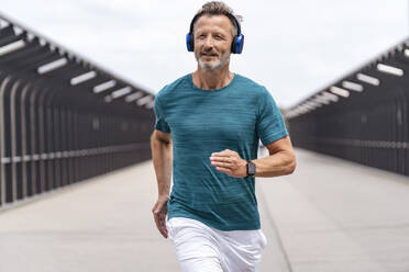 Sporty man wearing headphones and jogging - DIGF07493
