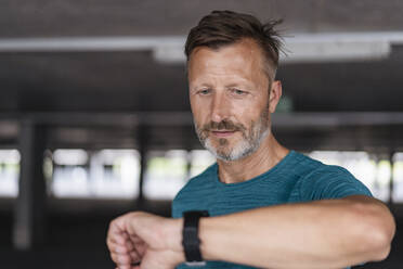 Portrait of a sporty man checking his smartwatch - DIGF07526