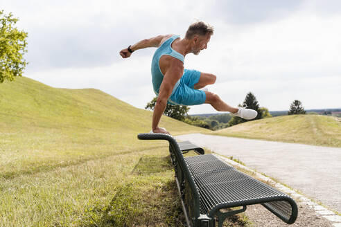 Sportlicher Mann springt über eine Bank im Park - DIGF07550