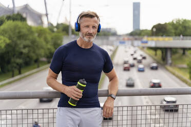 Sporty man with drinking bottle and headphones on a bridge - DIGF07553