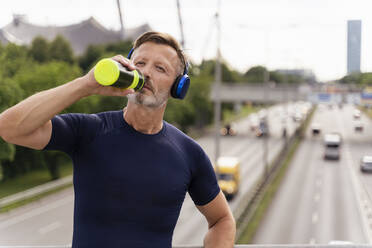 Sportlicher Mann mit Trinkflasche und Kopfhörern auf einer Brücke - DIGF07555