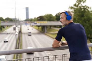 Sportlicher Mann steht auf einer Brücke und trägt Kopfhörer - DIGF07557