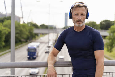 Sporty man standing on a bridge wearing headphones - DIGF07558