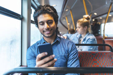 Porträt eines jungen Mannes, der mit dem Bus fährt und auf sein Handy schaut, London, UK - WPEF01585