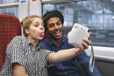 Porträt von Freunden, die Spaß haben, während sie ein Selfie mit einer Sofortbildkamera im Zug machen, London, UK - WPEF01598