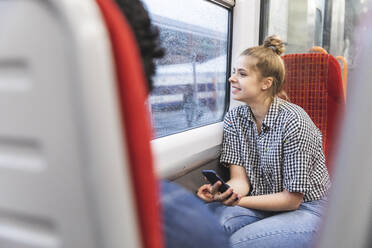 Smiling young man travelling by train with her boyfriend on rainy day looking out of window, London, UK - WPEF01604