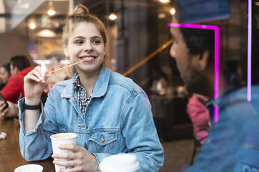 Porträt einer lächelnden jungen Frau in einem Café, die einen jungen Mann ansieht - WPEF01607