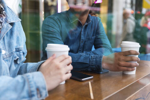 Hände halten Einwegbecher in einem Coffeeshop, Teilansicht, lizenzfreies Stockfoto