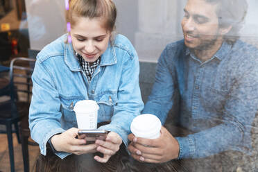 Junge Frau benutzt ihr Smartphone in einem Café, während ihr Freund sie beobachtet - WPEF01617