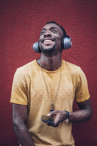 Porträt eines glücklichen jungen Mannes, der mit Kopfhörern und Smartphone Musik hört, lizenzfreies Stockfoto