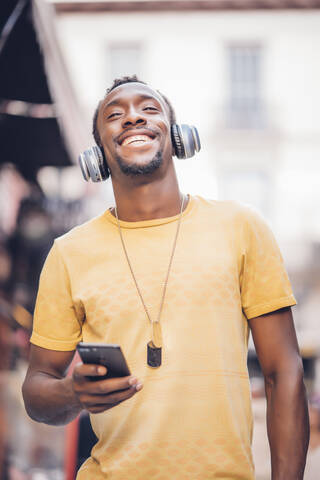 Porträt eines glücklichen Mannes, der mit Kopfhörern und Smartphone Musik hört, lizenzfreies Stockfoto