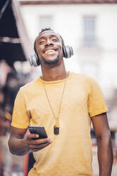 Porträt eines glücklichen Mannes, der mit Kopfhörern und Smartphone Musik hört - OCMF00490