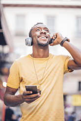 Porträt eines glücklichen Mannes, der mit Kopfhörern und Smartphone Musik hört - OCMF00492