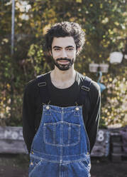 Portrait of smiling man wearing denim dungarees in garden - VGPF00061