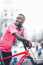 Glücklicher junger Mann mit E-Bike in der Stadt - OCMF00495
