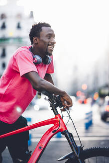 Glücklicher junger Mann mit E-Bike in der Stadt - OCMF00496