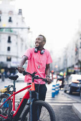 Glücklicher junger Mann mit E-Bike in der Stadt - OCMF00502