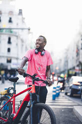 Happy young man with e bike in the city - OCMF00502