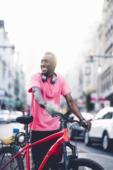 Lächelnder junger Mann mit E-Bike in der Stadt - OCMF00503