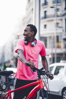 Lächelnder junger Mann mit E-Bike in der Stadt - OCMF00504