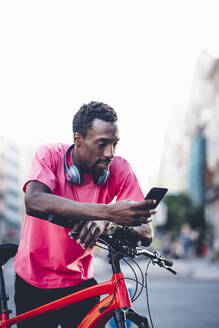 Junger Mann mit E-Bike und Smartphone in der Stadt - OCMF00505