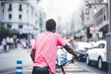 Rückansicht eines jungen Mannes mit E-Bike in der Stadt - OCMF00507