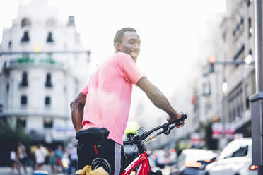 Lächelnder junger Mann mit E-Bike in der Stadt - OCMF00508