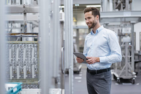 Lächelnder Geschäftsmann mit Tablet im Gespräch in einer modernen Fabrik - DIGF07578