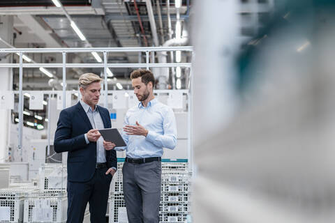 Zwei Geschäftsleute mit Tablet im Gespräch in einer modernen Fabrik, lizenzfreies Stockfoto