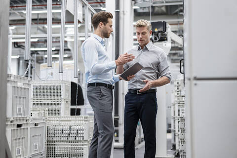 Zwei Geschäftsleute mit Tablet im Gespräch in einer modernen Fabrik, lizenzfreies Stockfoto