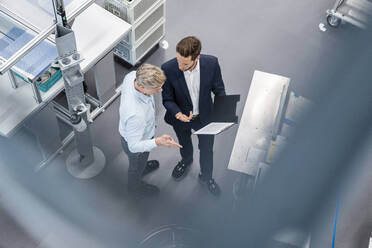 Zwei Geschäftsleute mit Klemmbrett im Gespräch in einer Fabrik - DIGF07590