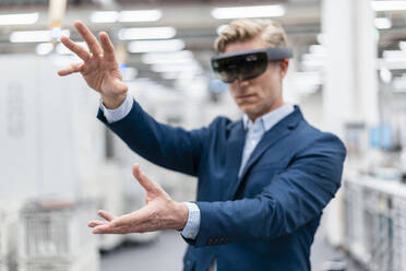 Businessman wearing AR glasses in a modern factory - DIGF07622