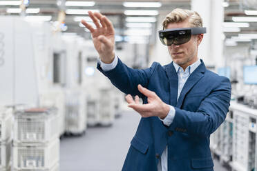 Businessman wearing AR glasses in a modern factory - DIGF07623