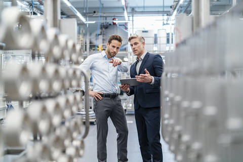 Zwei Geschäftsleute mit Tablet im Gespräch in einer modernen Fabrik, lizenzfreies Stockfoto