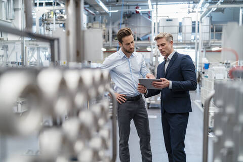 Zwei Geschäftsleute mit Tablet im Gespräch in einer modernen Fabrik, lizenzfreies Stockfoto