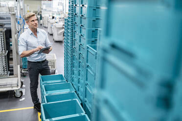 Businessman using tablet in a factory hall with boxes - DIGF07667