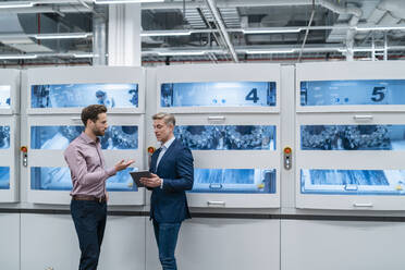 Zwei Geschäftsleute mit Tablet im Gespräch an einer Maschine in einer modernen Fabrik - DIGF07679
