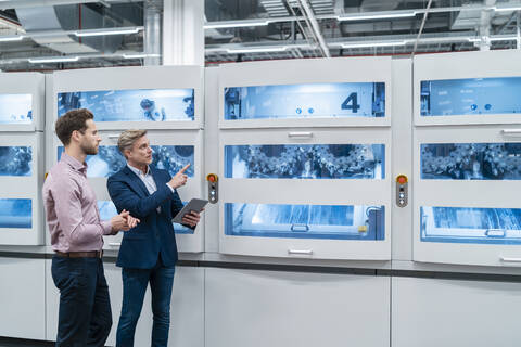 Zwei Geschäftsleute mit Tablet im Gespräch an einer Maschine in einer modernen Fabrik, lizenzfreies Stockfoto