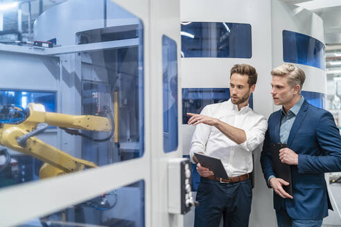 Zwei Geschäftsleute im Gespräch mit einem Roboter in einer modernen Fabrik - DIGF07698