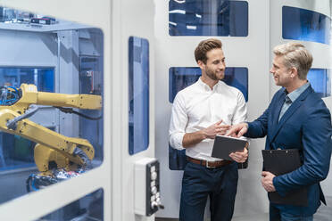 Zwei Geschäftsleute im Gespräch mit einem Roboter in einer modernen Fabrik - DIGF07699