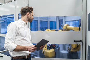 Geschäftsmann mit Tablet und Blick auf Roboter in einer modernen Fabrik - DIGF07703