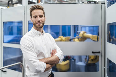 Portrait of a smiling businessman in front of a robot in a modern factory - DIGF07704