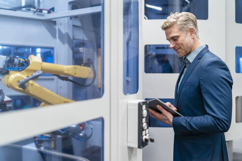 Geschäftsmann mit Tablet an einem Roboter in einer modernen Fabrik - DIGF07705