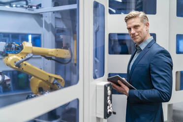 Portrait of a confident businessman in front of a robot in a modern factory - DIGF07706