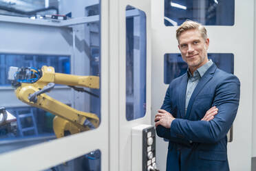 Portrait of a confident businessman in front of a robot in a modern factory - DIGF07707