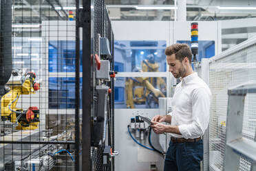 Businessman using tablet at a robot in a modern factory - DIGF07716