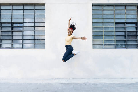 Glückliche junge Frau, die vor einer weißen Wand in die Luft springt, lizenzfreies Stockfoto