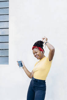 Young woman listening music with headphones and earphones singing and dancing in front of white wall - SODF00006