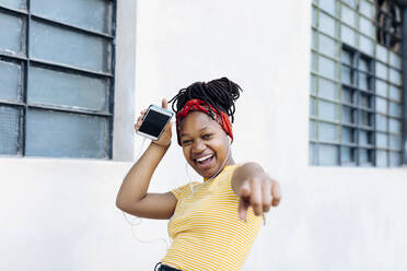 Portrait of excited young woman listening music with headphones and earphones in front of white wall - SODF00008